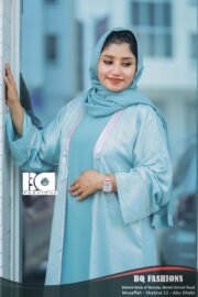 Young woman modeling light blue overcoat abaya with white lace trim detailing and matching blue hijab, standing indoors by glass entrance